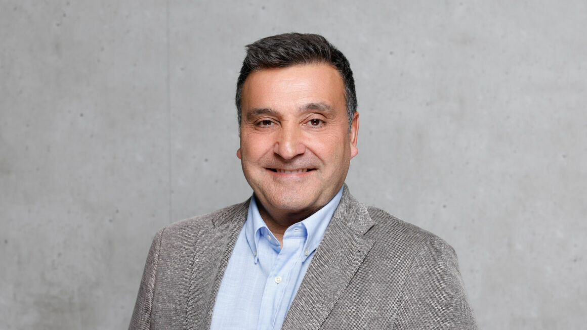 The picture shows Matías Carnero Sojo in front of a gray concrete wall. He is wearing a suit and a shirt.