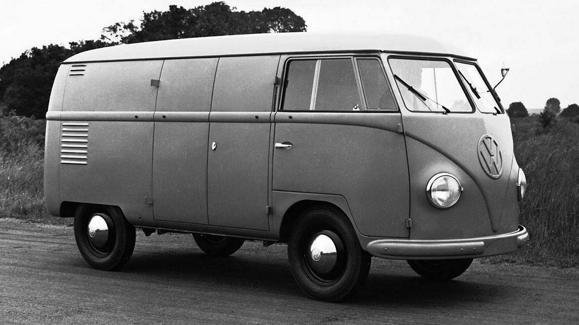 Schwarz-weiß-Foto eines klassischen VW Transporters mit geschlossenem Laderaum, stehend auf einer Straße mit Bäumen im Hintergrund.